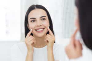 Woman smiling while looking in the mirror at her balanced facial features due to facial balancing treatments